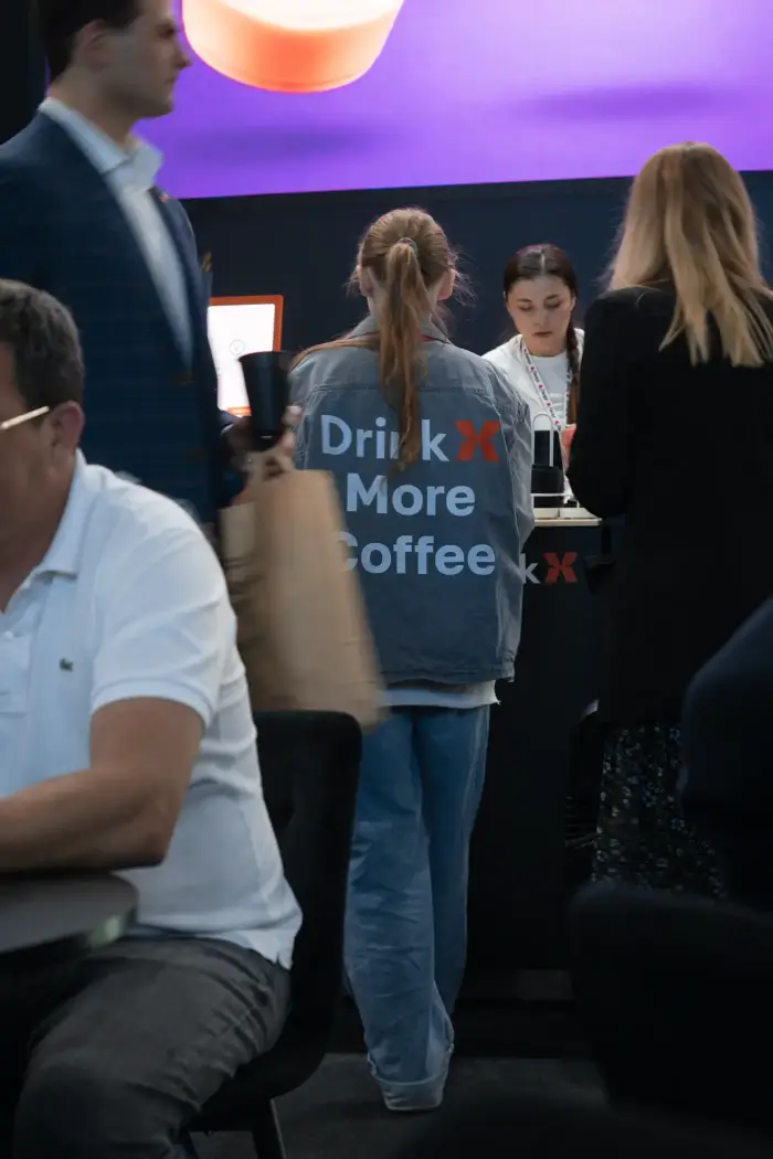 Посетители выставки у стойки DrinkX, на куртке надпись Drink More Coffee