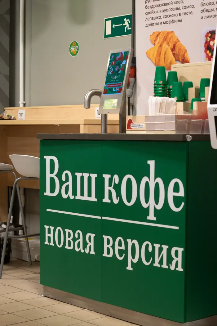Кофейная зона с зелёной стойкой в сетевом магазине, на столешнице кран и экран заказа