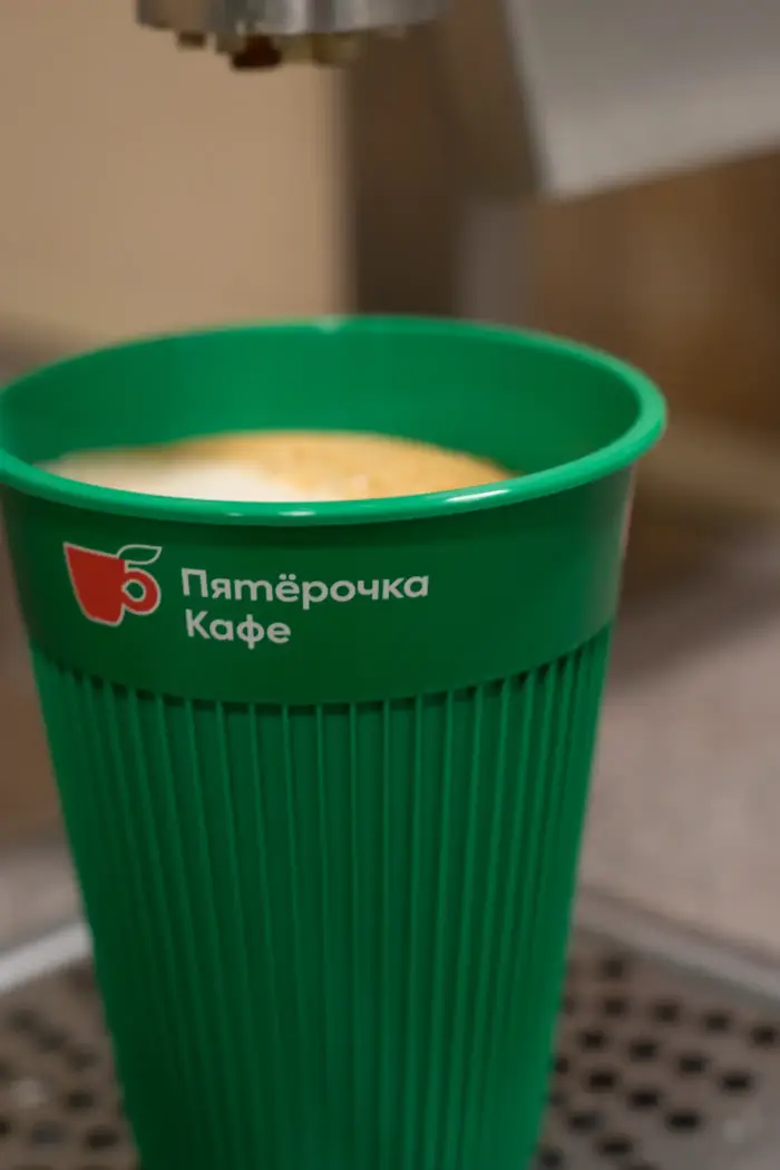 Зелёный стакан с капучино под краном кофейной станции