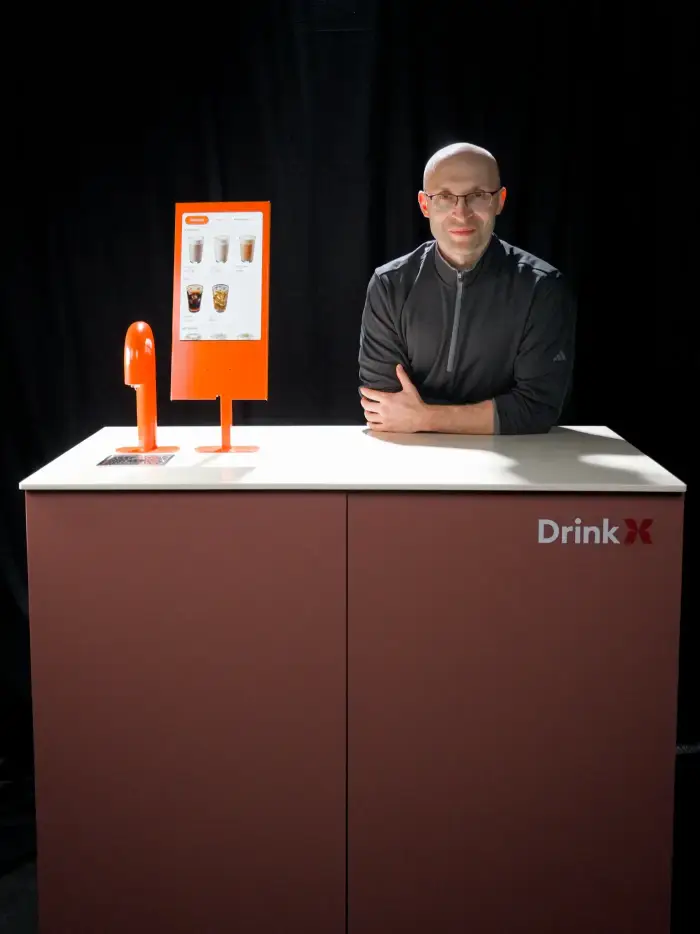 Станция DrinkX целиком на тёмном фоне: бордовая стойка, оранжевый кран и экран